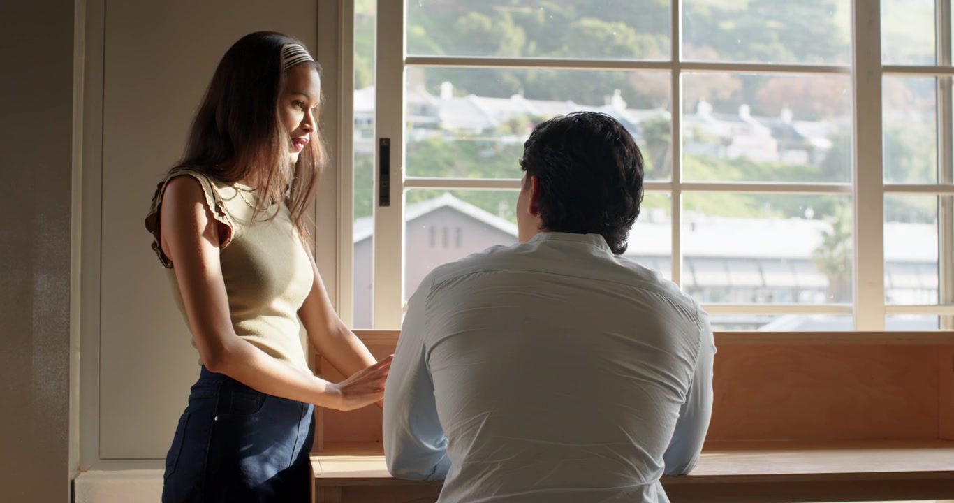 Asian man sitting on bench African American woman leaning bonding by window with headband gesturing