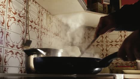 person stirs food from a smoking pan with a wooden spoon