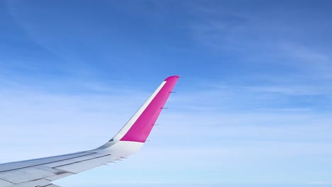 a vibrant pink airplane wing set against a vast, clear blue sky with scattered clouds.