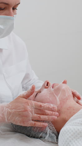 esteticista aplicando una máscara hidratante relajante en el rostro de una mujer joven adulta para rehidratar la piel del rostro