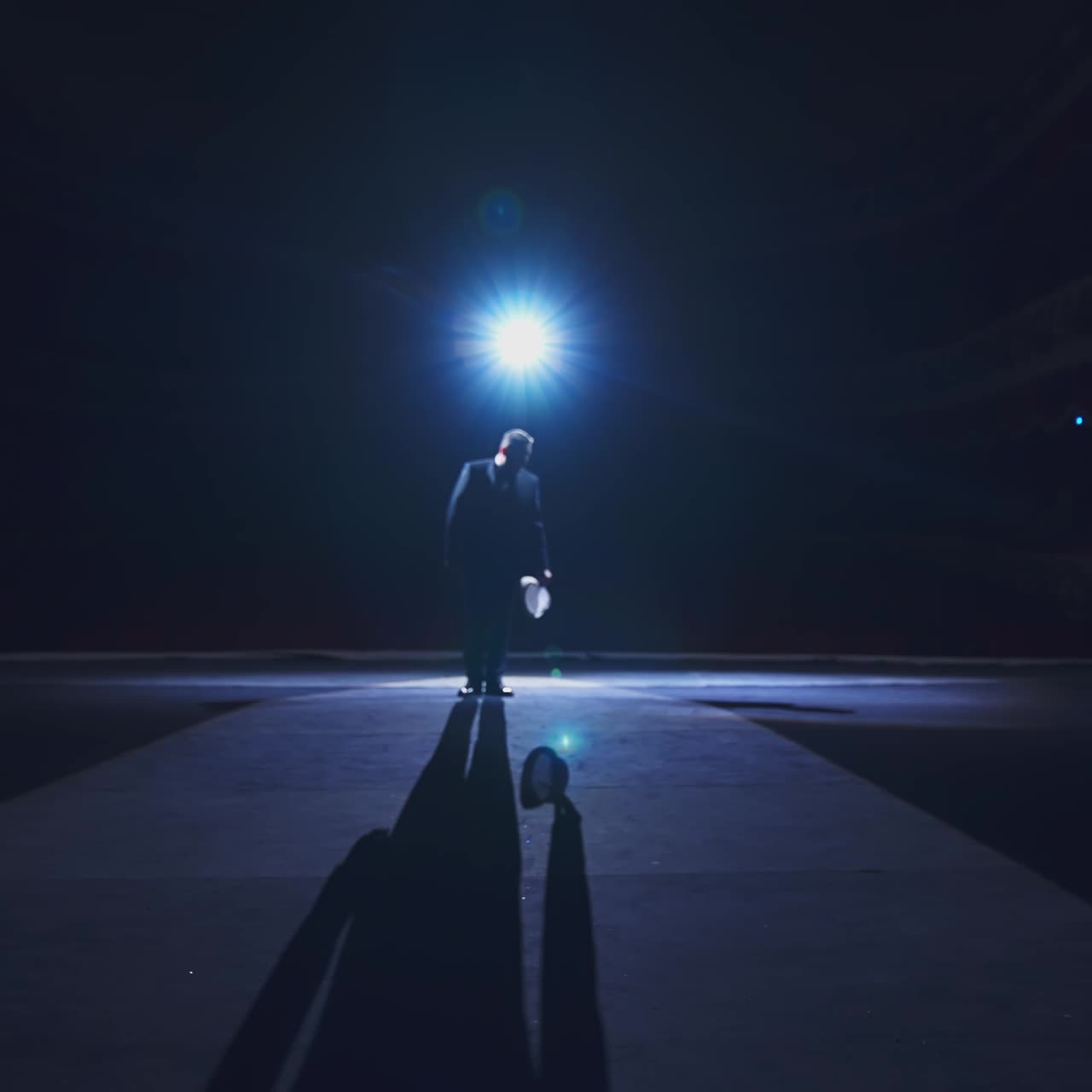 Elegant man on stage. Dark silhouette of a stylish man wearing hat performing on the scene in theatre at spotlight. View from the stage.