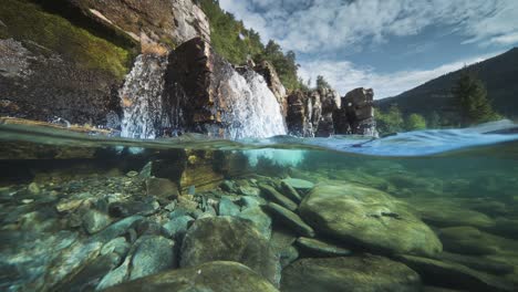 a shallow river with rocky shores and transparent waters, with a waterfall in the background