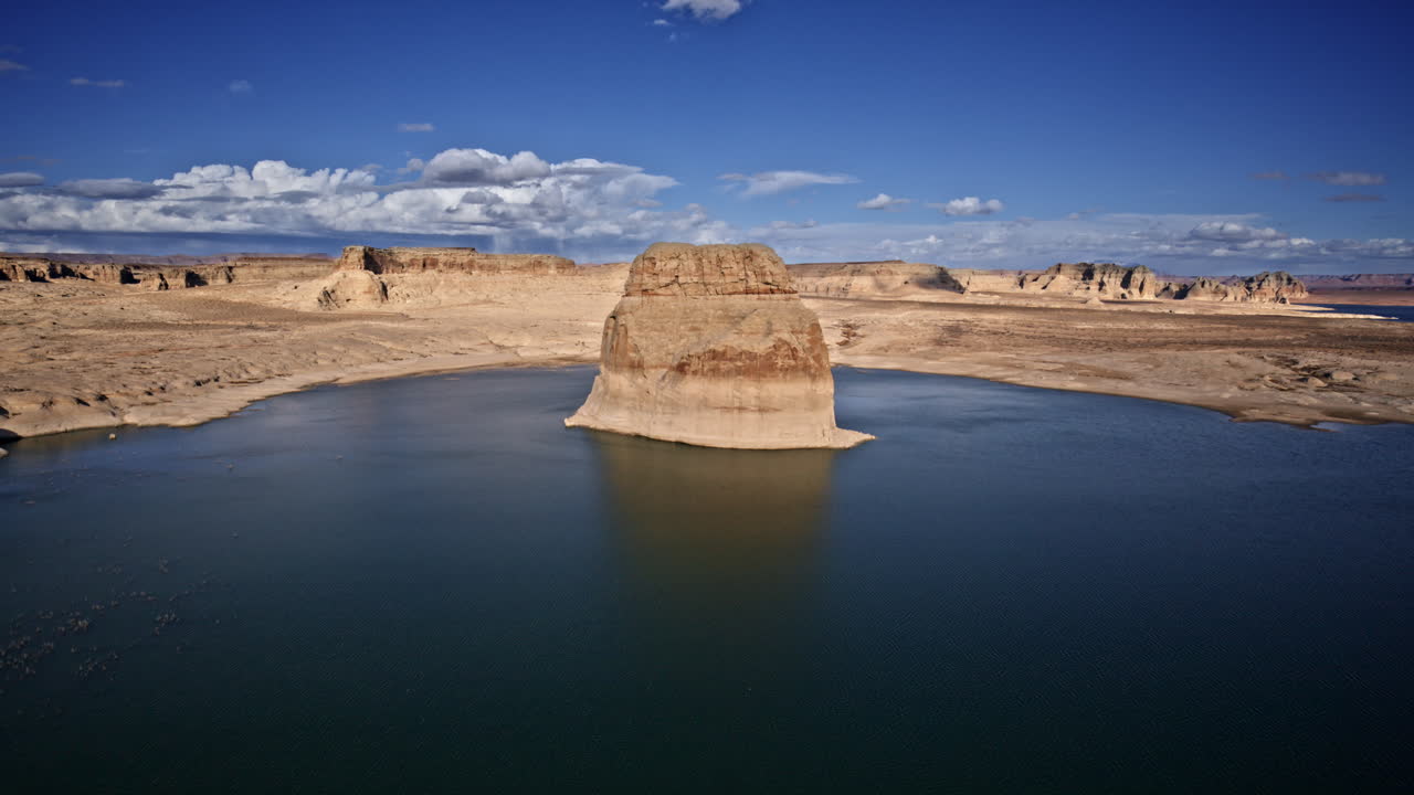 Drone footage revealing a striking lone rock in the waters of Lake Powell, with a stunning desert canyon backdrop.