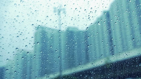 Gotas-De-Lluvia-En-La-Ventana-De-La-Superficie-De-Vidrio-Con-Fondo-De-Paisaje-Urbano-Borroso---Primer-Plano