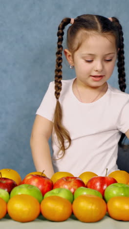 children at table with fruit. portrait of little girl sitting at table with fruit. vertical video