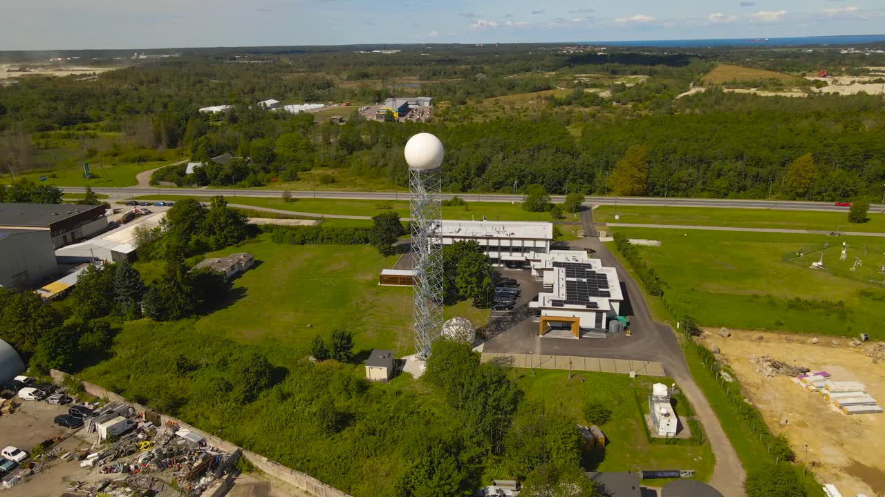 Aerial drone footage orbiting around a weather station with a large radome radar or dome on a large antenna tower that is metering climate and brodcasting data during a summer sunny day, highway seen