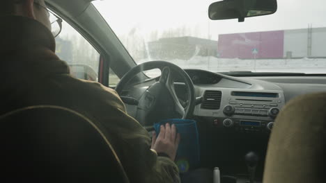 rear view of man cleaning steering wheel with blue cloth inside parked car during bright winter day showing dashboard, frosted window, and snowy outdoor environment through windshield