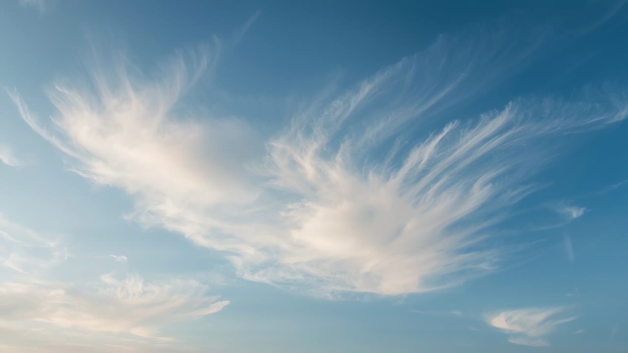 Blowing upper wind shaping cirrus clouds, stretching strands across late-evening sky, warm horizon