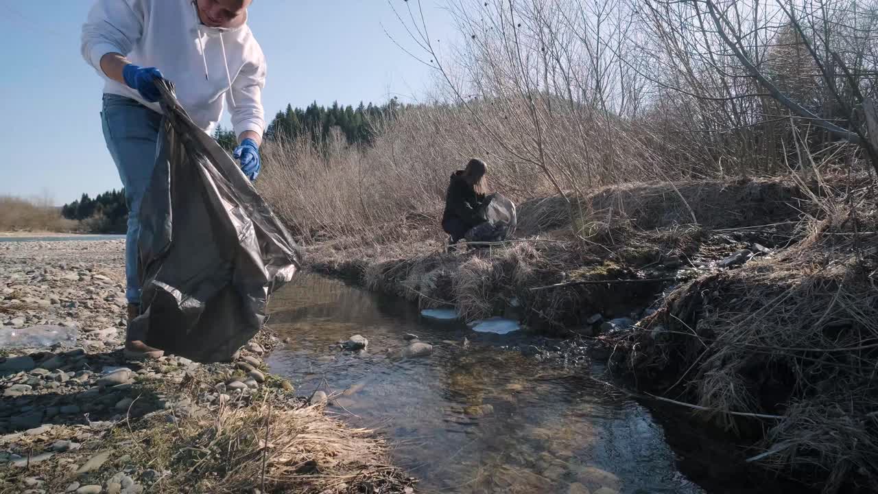 Holdarbejde med oprydning af plastik på stranden. Frivillige samler affald i en affaldspose. Koncept for plastikforurening og miljøproblemer. Frivillig oprydning af naturen for plastik. Gør planeten grønnere.