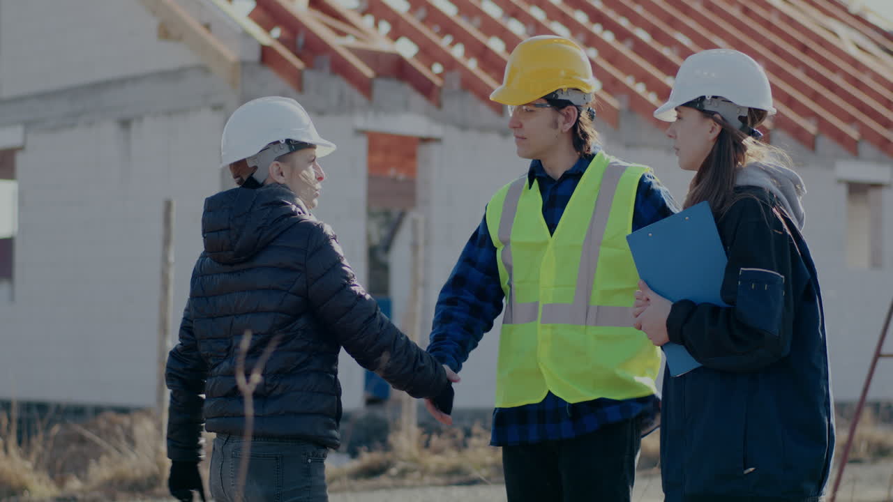 Confident female civil engineer discussing while greeting building contractor and worker with handshakes at incomplete construction site