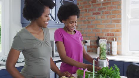 Happy-african-american-mother-and-daughter-preparing-healthy-drink,-making-video-using-camera