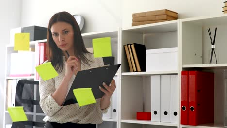 mujer de negocios haciendo notas en documentos de pie cerca de la pared de vidrio