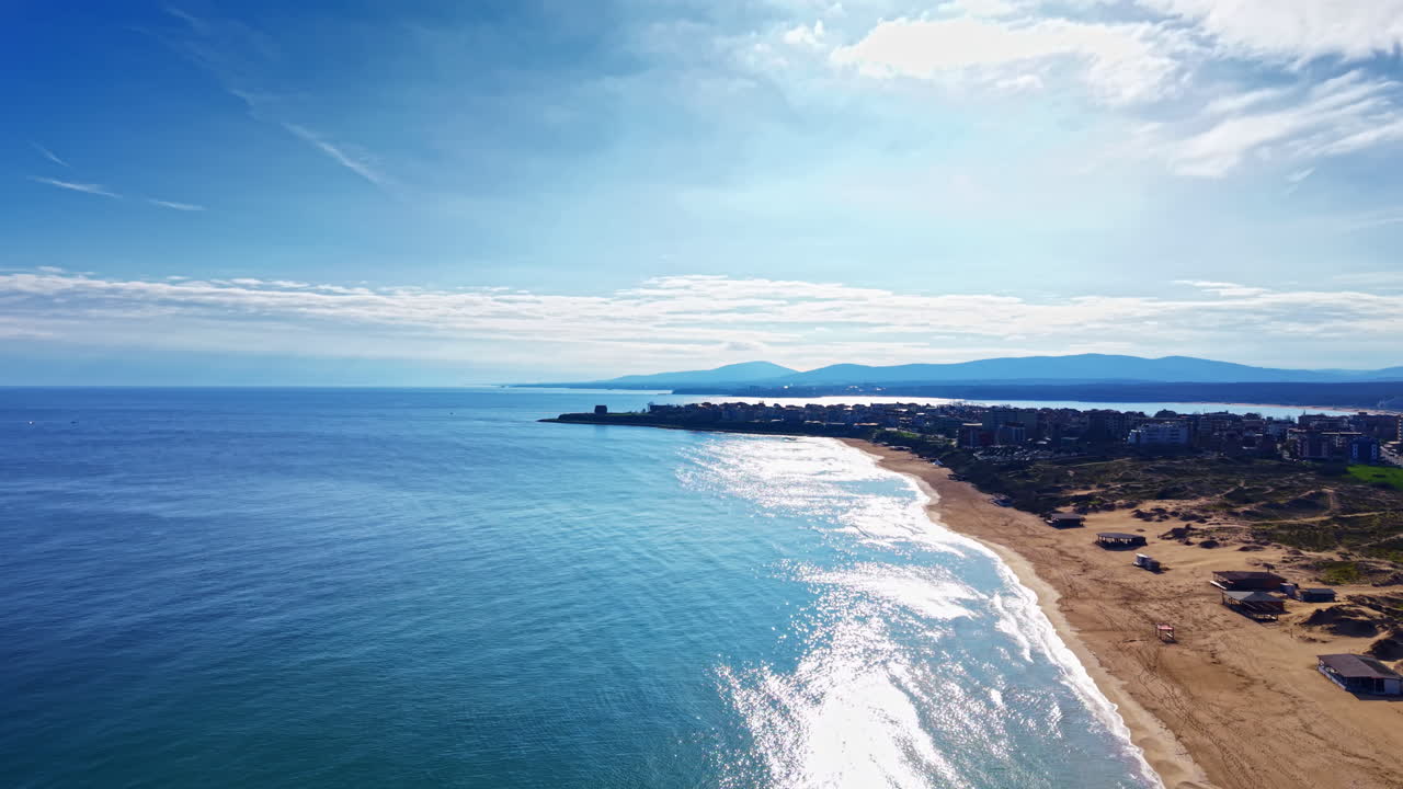 穏やかな海辺の風景。広大な海、砂浜、そして澄んだ青空の下に遠くの山々を捉えています。