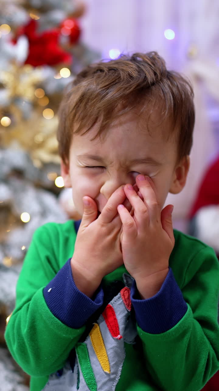 Thoughtful baby boy sitting in front of camera. Lovely toddler near the Christmas tree at home. Blurred backdrop. Vertical video