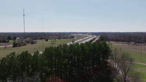 Drone-shot-of-a-highway-surrounded-by-groupings-of-trees-and-billboards-under-a-clear-sky