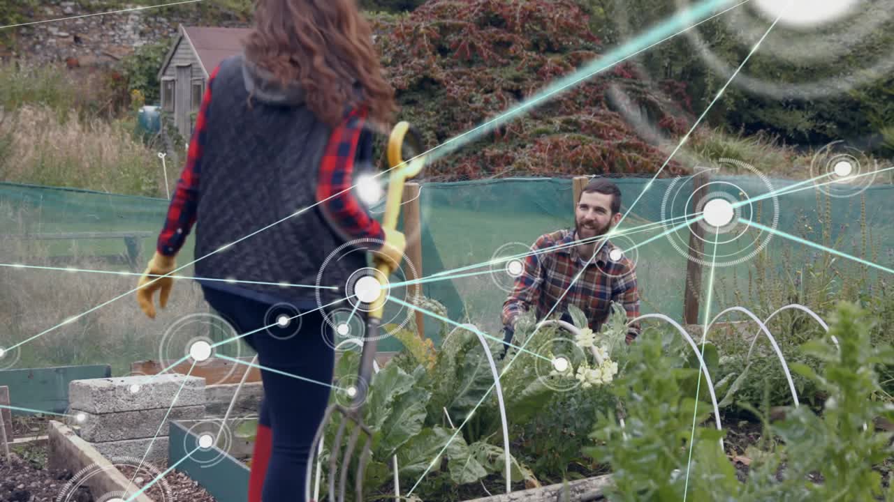 Donna che spinge una forca da giardino nel terreno con il piede, innescando una sovrapposizione di nodi mentre il partner diserba per la piantumazione.