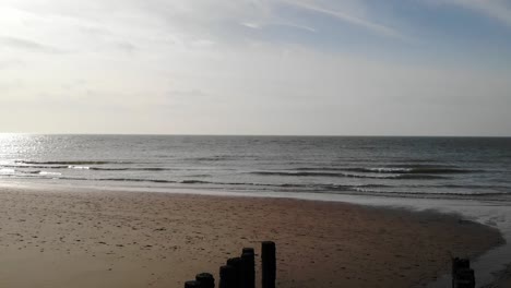 Playa-Tranquila-Con-Olas-Ondulantes-Y-Viejos-Pilotes-De-Madera-En-La-Costa-En-Brouwersdam,-Países-Bajos---Toma-Aérea-De-Drones