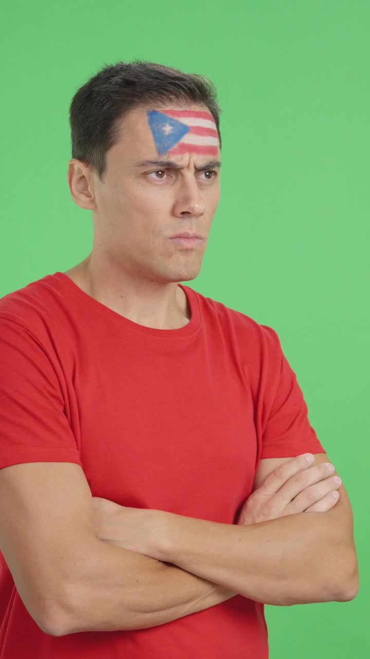 Man with puerto rican flag painted looking away with serious expression