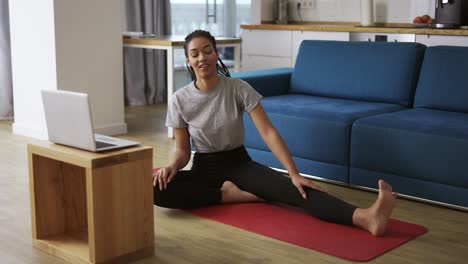 mujer afroamericana deportiva que hace ejercicio, haciendo ejercicios de estiramiento en la alfombra de yoga mientras ve un video de fitness