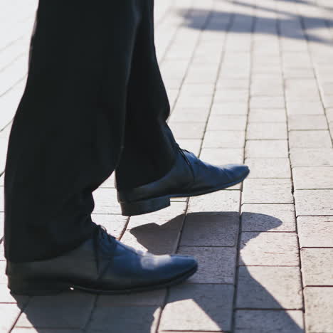 feet of the businessman walking outdoors. legs of a man in black trousers and shoes walking nervously up and down the street. close-up.