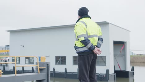 seaman with clasped hands looking over a ship in the harbour