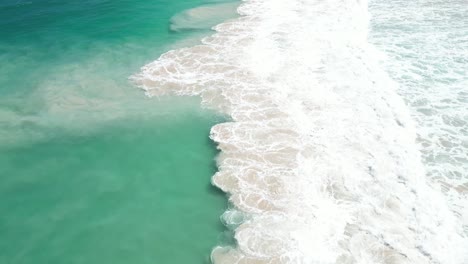 aerial view of turquoise ocean waves crashing on white sand beach
