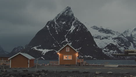 picturesque view of a lighted small cabin with background of olstinden mountain at twilight in the village of sakrisoy, lofoten islands norway - wide shot