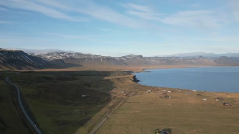 Calm-village-by-fjord,-winding-road-and-wispy-clouds,-summer-in-Iceland