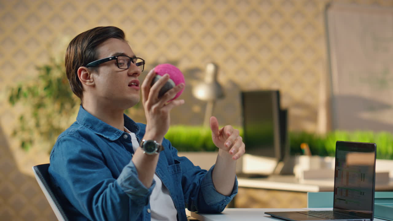 미소 짓는 남자가 컴퓨터 작업장 근접에서 공을 던지고 있습니다. 프리랜서가 장난감을 잡습니다.