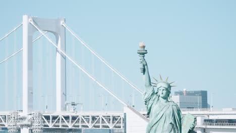 replica of statue of liberty in odaiba with rainbow bridge crossing tokyo bay in minato, tokyo, japan