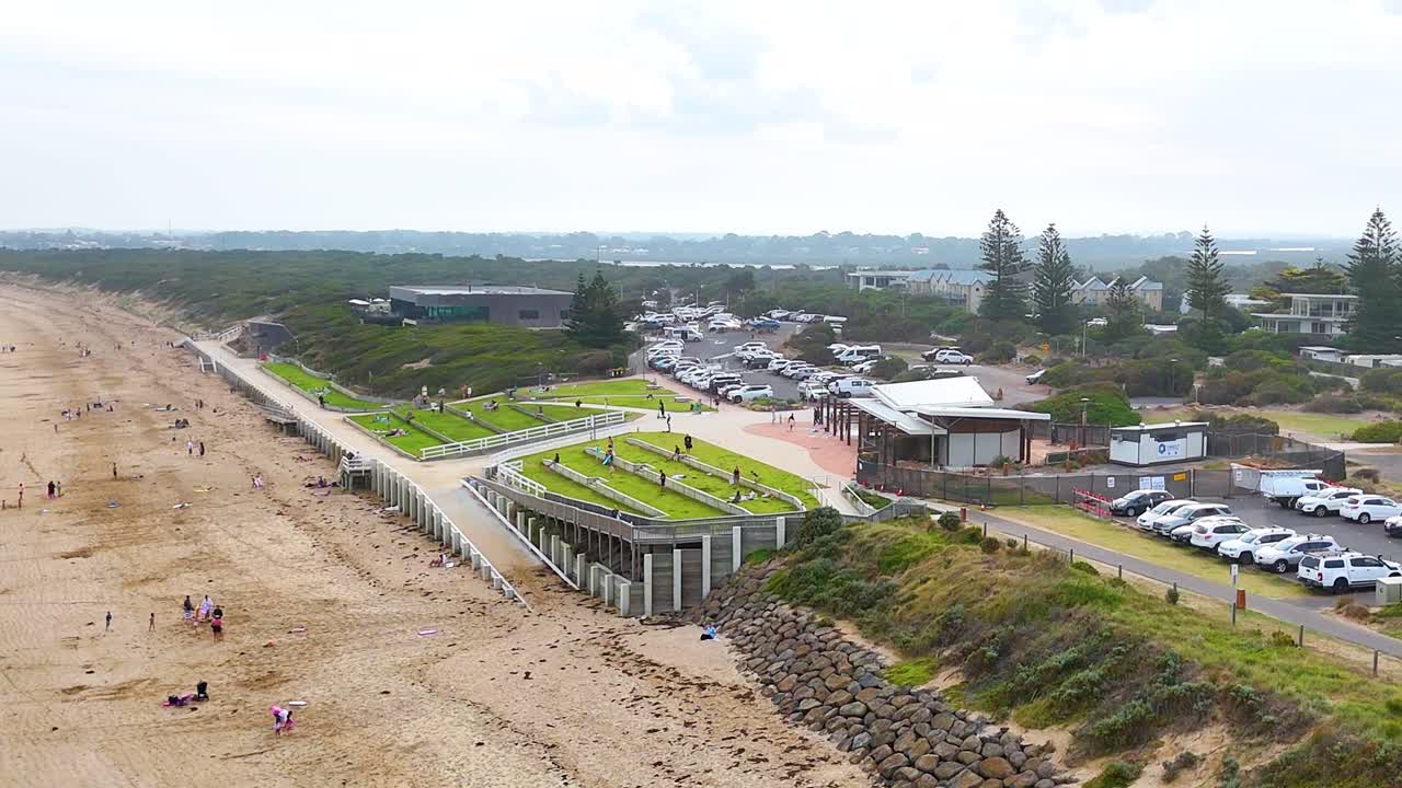 Aerial footage captures Ocean Grove beach, parking area, and nearby structures under bright daylight, showcasing a serene coastal environment