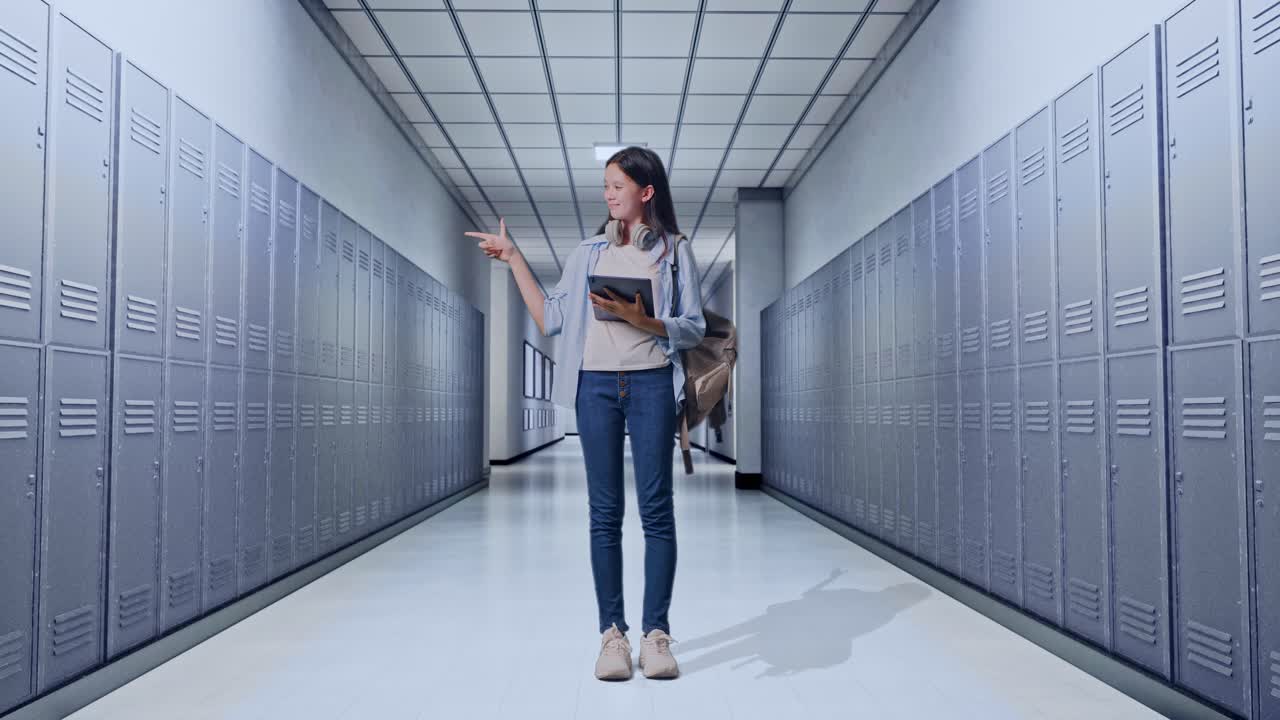 cuerpo lleno de estudiante adolescente asiática con una mochila usando una tableta y apuntando a un lado mientras estaba de pie en el pasillo