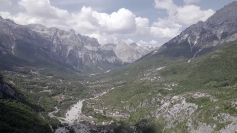 Frontal-drone-video-advancing-inside-the-theth-valley-in-albania,-over-the-river-Lumi-i-thethit-with-hardly-any-water,-with-Mount-Korab-in-the-background