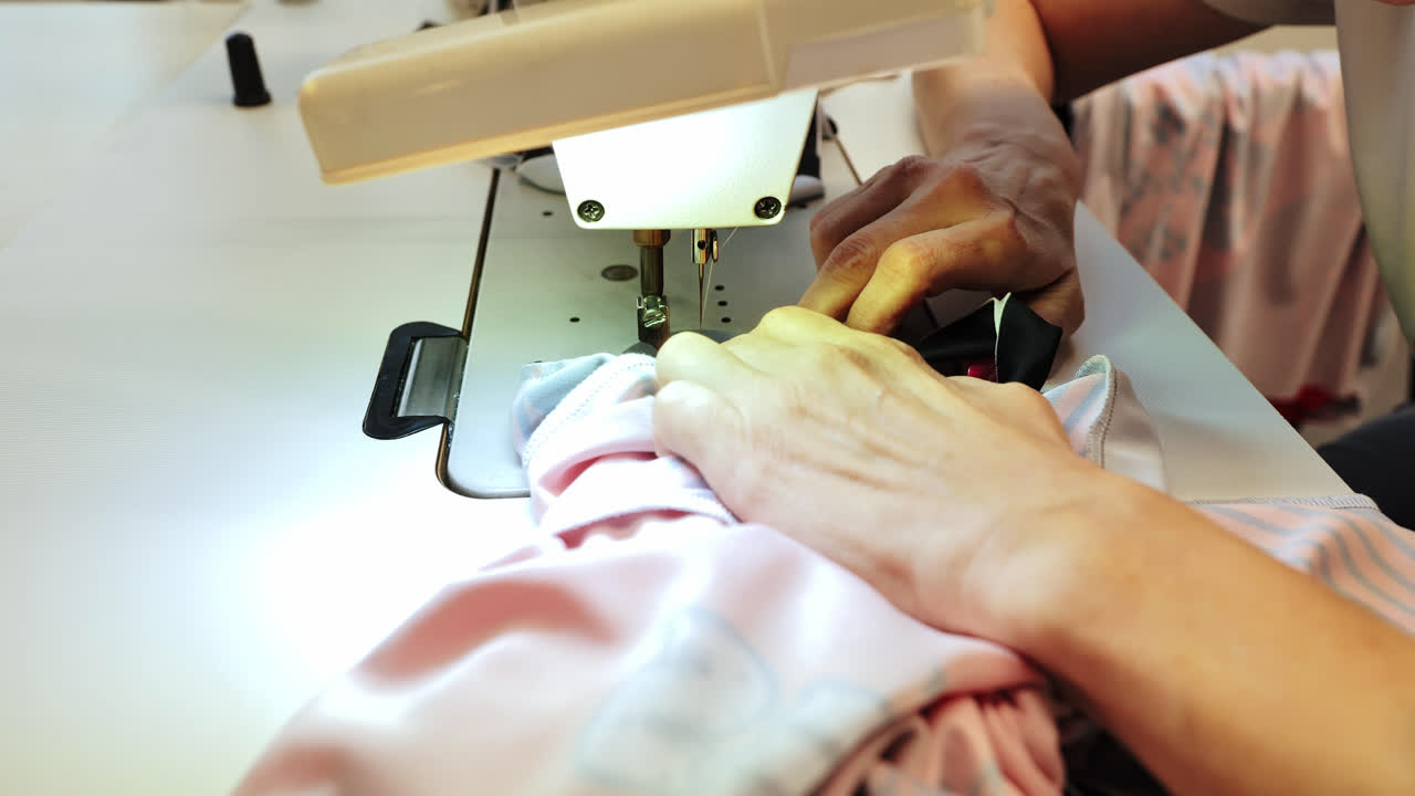 Woman carefully sews sportswear fabric on machine, viewed from side, zooming out