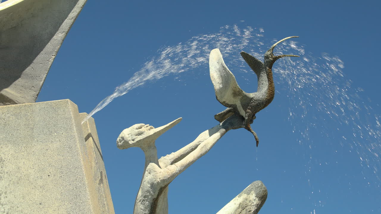 A beautiful water fountain with cascading water in Victoria Square, Adelaide, Australia. This video captures the intricate details of the fountain's sculpture against a clear blue sky.