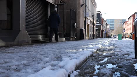 Man-walking-on-snowy-city-street-on-sunny-day,-Sheffield,-low-angle