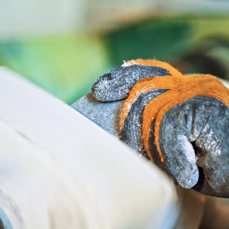 hand of a worker in protective glove is holding stone at the electric machine. man is polishing stone on the circular machine at factory. close-up.
