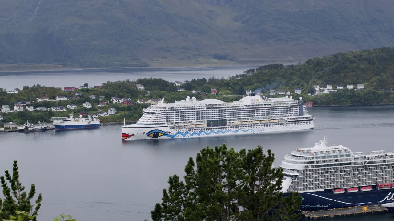 Two cruise ships sail past a scenic coastal village surrounded by mountains and calm waters