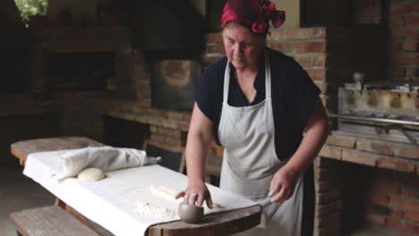 old woman baker flattens the shoti bread dough with hands, puts some flour and oil before putting it inside the traditional round clay oven