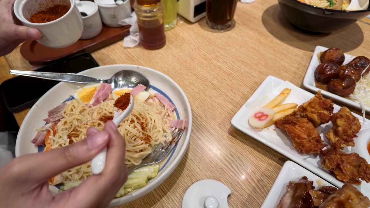프라이드 치킨과 타코야끼 옆에서 고춧가루로 라면을 양념하는 손의 클로즈업 샷