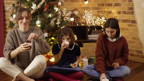 Madre-E-Hijas-Pequeñas-Bebiendo-Cacao-Con-Galletas-En-El-Suelo-En-Nochebuena-En-Casa