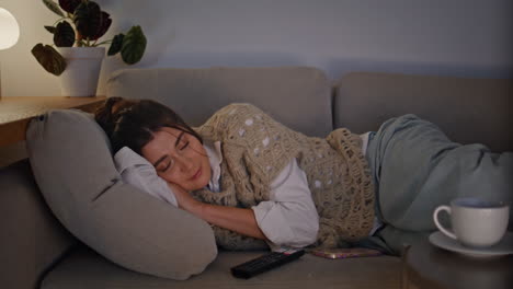 sleepy woman lounging sofa looking tv at evening home. lady switching channels