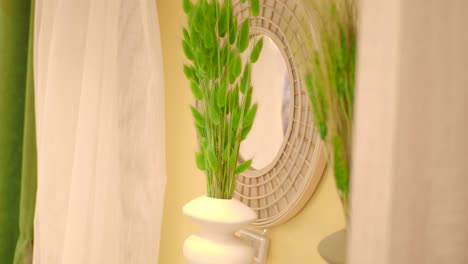 green decorative plants in a white vase with a round mirror and curtains