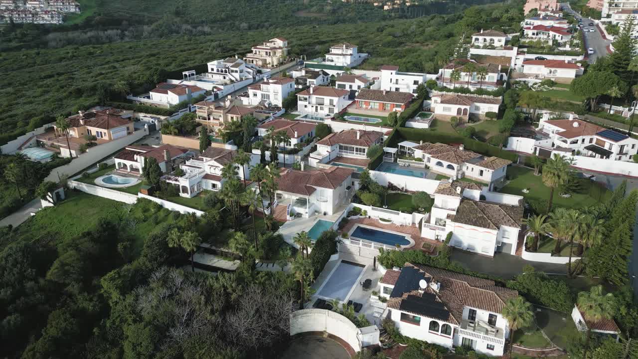 Vídeo aéreo que captura un barrio mediterráneo de villas y vegetación en la Costa del Sol, con montañas y costa en la distancia