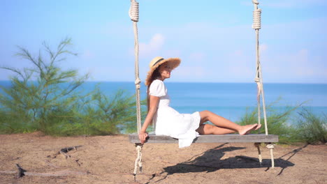 a woman sitting on a large wooden swing with the ocean in the background gently rocks back and forth