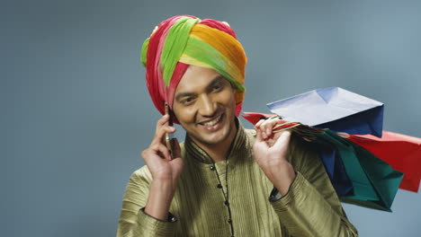 close-up view of cheerful indian man in traditional clothes and turban talking on the phone and holding shopping bags