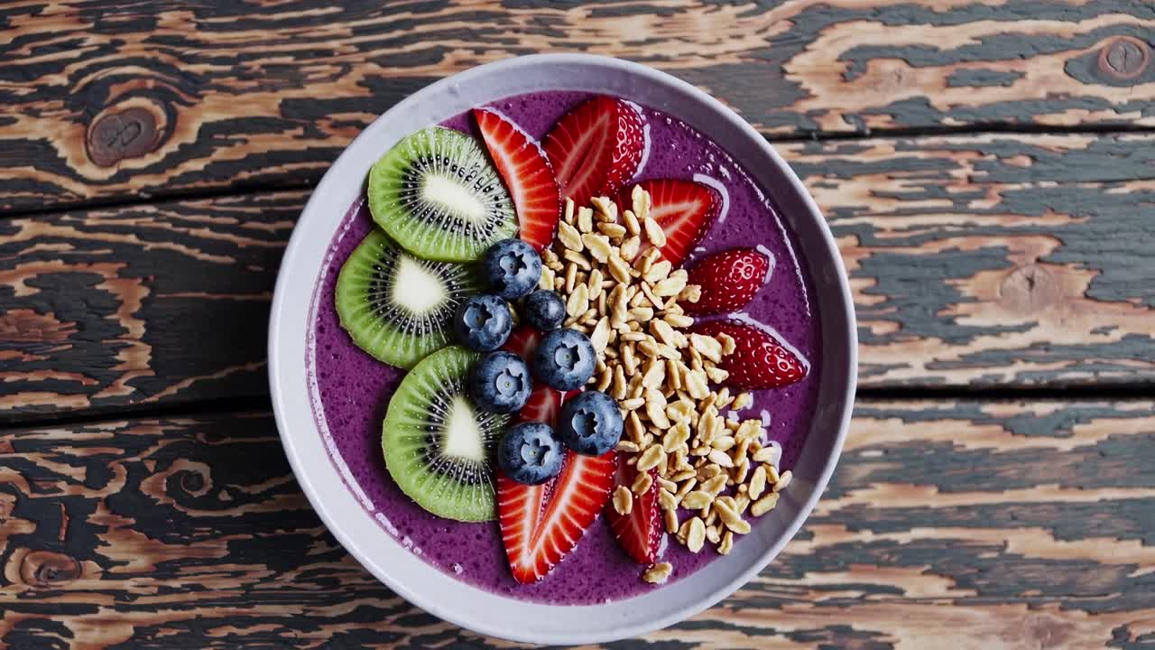 Top-down view of a vibrant smoothie bowl with fruits and granola on rustic wood