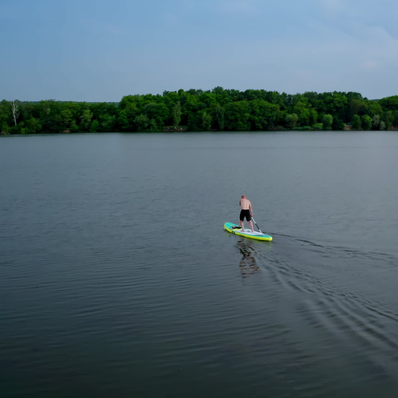 Active adventure on water. Sportsman training on water while standing on a board with oars on the background of beautiful summer landscape. Extreme sport