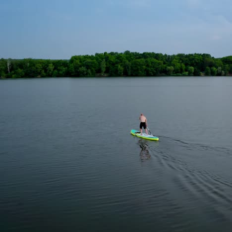 active adventure on water. sportsman training on water while standing on a board with oars on the background of beautiful summer landscape. extreme sport