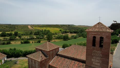campanario de ladrillo de la iglesia con nido de cigüeñas y verdes tierras de cultivo en el fondo
